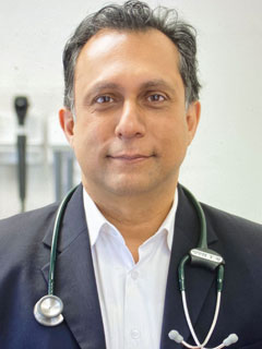 Dr. Alykhan Abdulla, seen from the chest up, wearing a stethoscope around his neck, a suit, short black hair, and smiling
