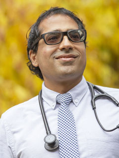 Dr. Amit Arya, seen from the chest up, wearing a stethoscope around his neck, dress shirt and tie, glasses, short black hair, and smiling
