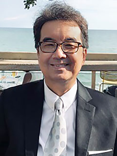Dr. Danny Yeung, seen from the chest up, wearing a black blazer, short grey hair, glasses, and smiling
