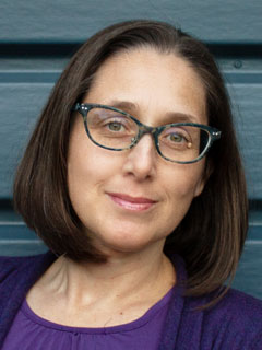 Dr. Kate Miller, seen from the shoulders up, wearing a purple shirt, short brown hair, glasses, and smiling