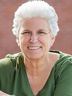 Dr. Kerry Beal, seen from the chest up, wearing a green blouse, short white hair, and smiling