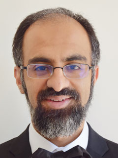 Dr. Mohamed Alarakhia, seen from the neck up, with black hair and bear, glasses, and smiling
