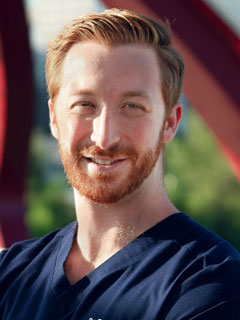 Dr. Russell Bahar, seen from the chest up, wearing blue scrubs, short red hair and beard, and smiling