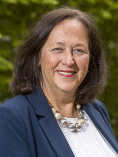Dr. Susan Coish, seen from the chest up, wearing a blue blazer, chunky necklace, short brown hair, and smiling
