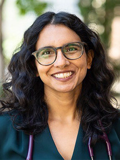 Dr. Tara Kiran, seen from the chest up, wearing a stethoscope around her neck, curly black hair, glasses, and smiling 