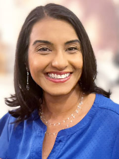 Dr. Zahra Bardai, seen from the chest up, wearing a blue blouse, short black hair, and smiling 