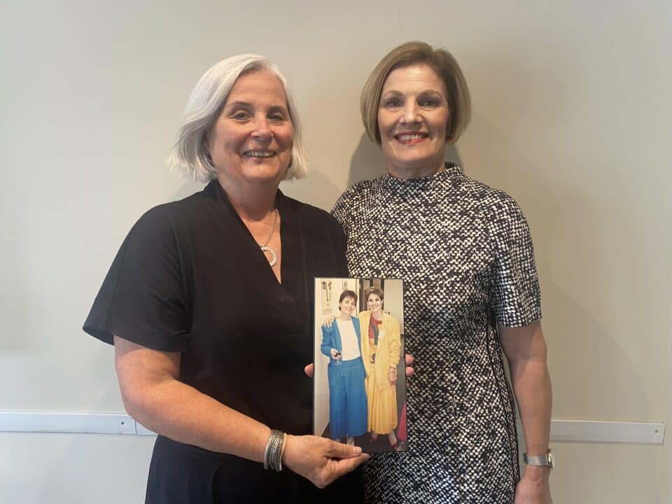 Brenda Copps and Jean Mullens holding up an image of themselves from years before.